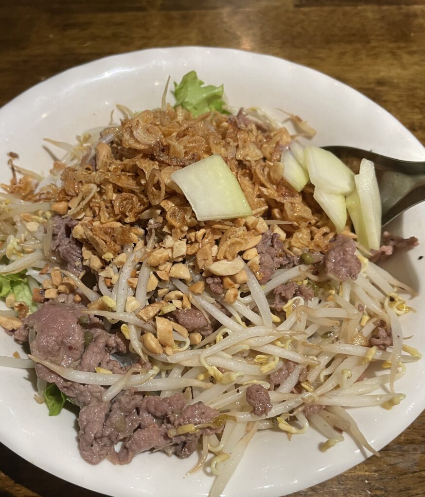 a beef salad served with papaya, sprouts, nuts, beef and more