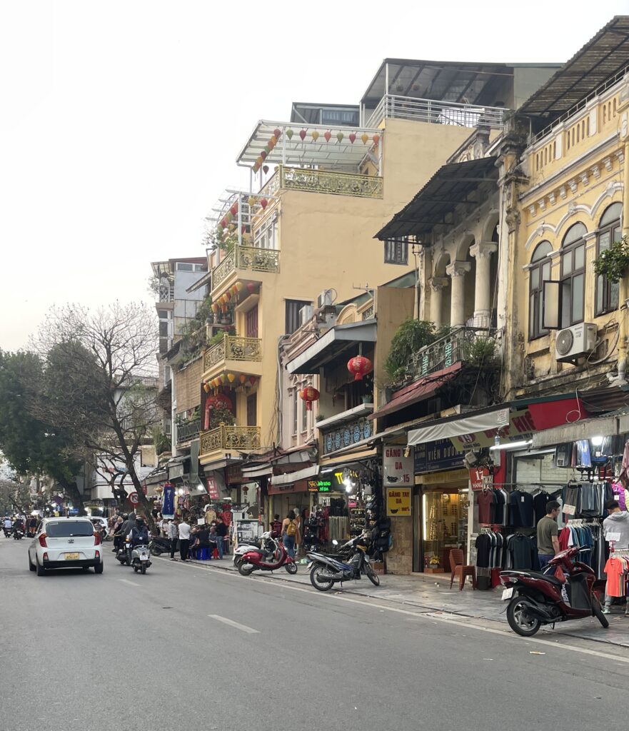 a picturesque street with nice buildings and locals walking by in Hanoi