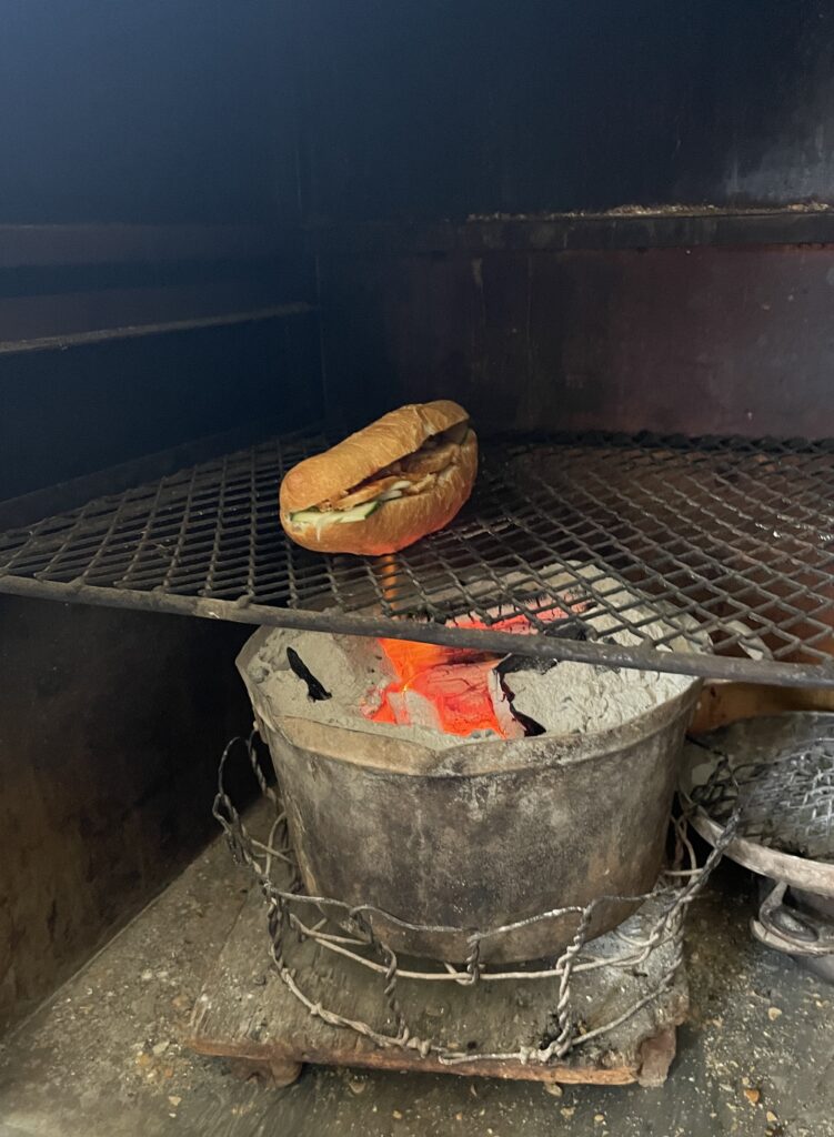 a banh mi sandwich being heated under hot charcoal fire
