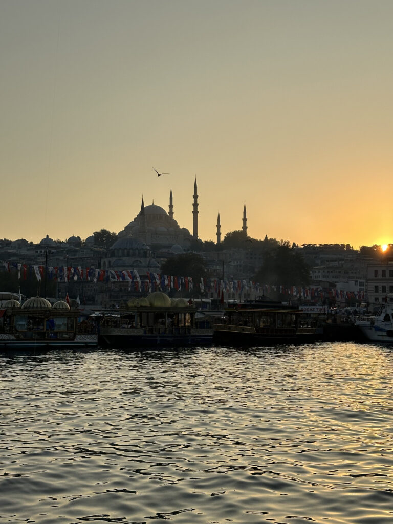 Golden hour river view in Istanbul with a mosque silhouetted at sunset and stunning skies casting warm light over the city.
