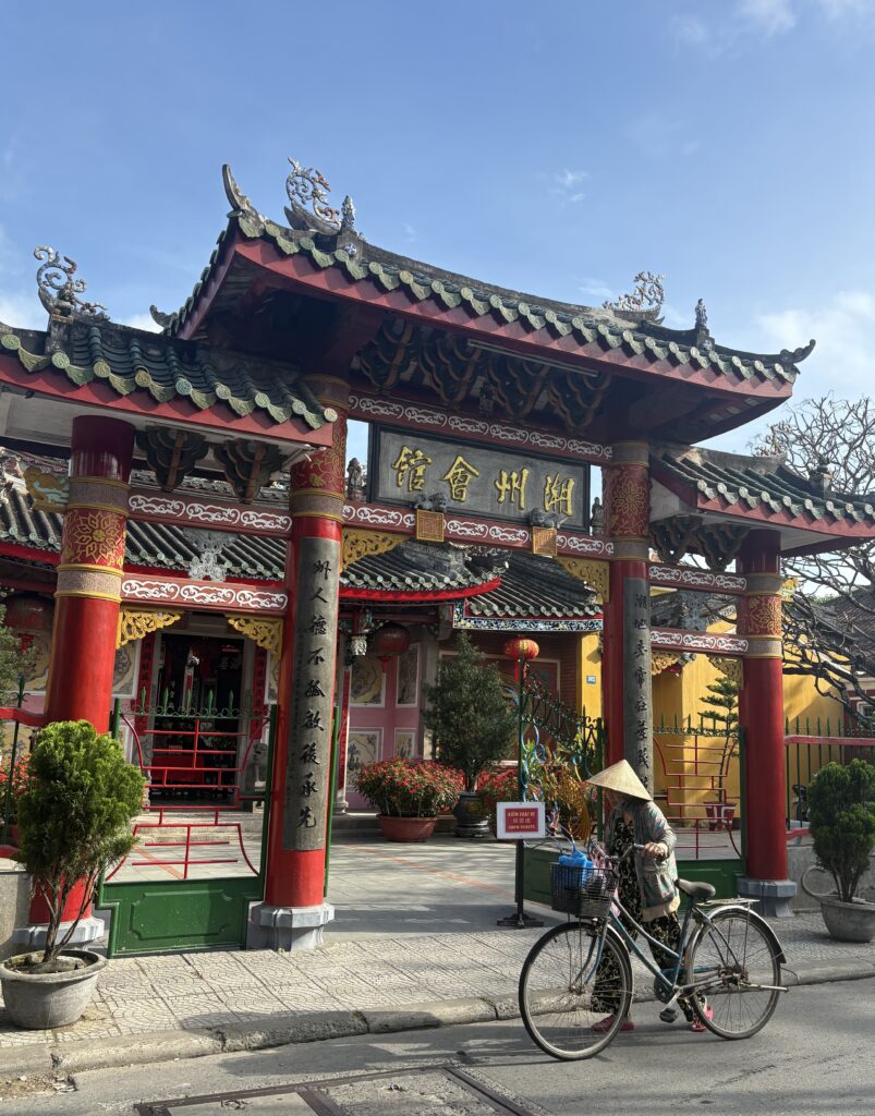 a woman biking by an old Chinese temple in Hoi An, Vietnam
