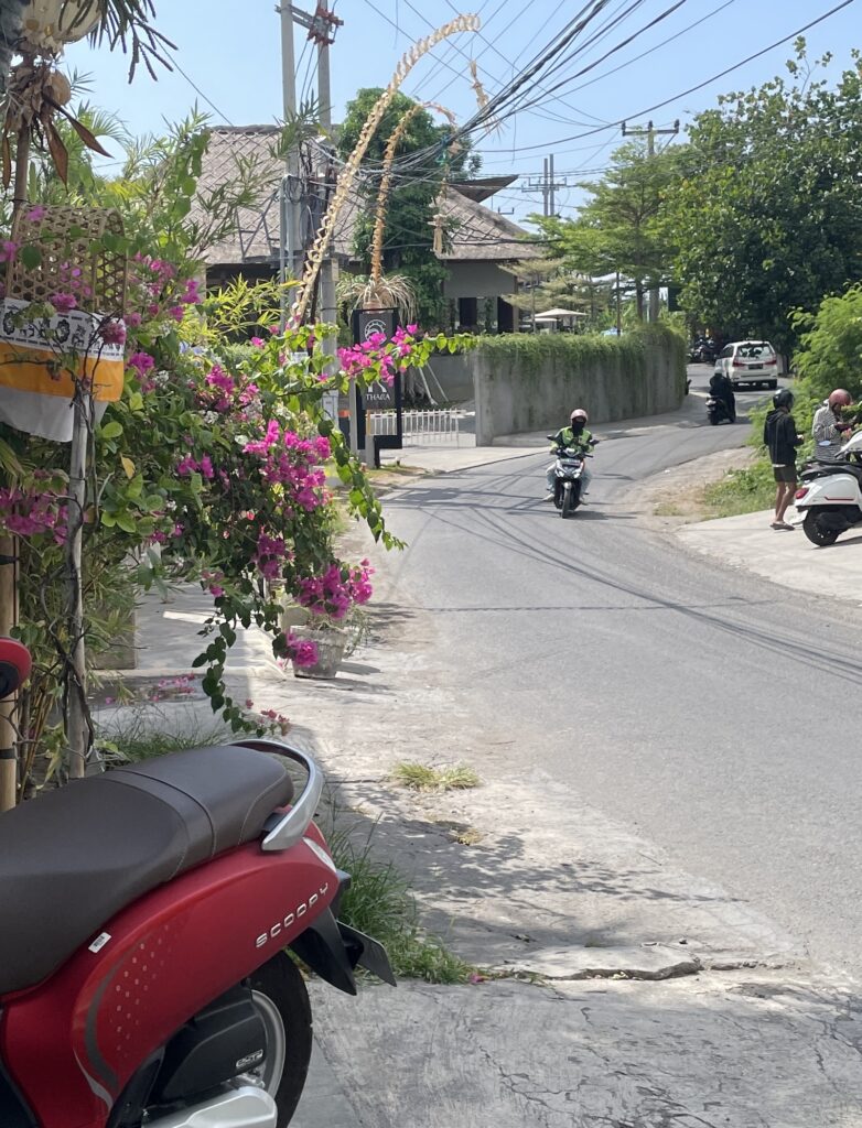 Scooter rider navigating a Bali street with a Grab driver in the background, capturing the island’s everyday scooter culture and ride-share presence.