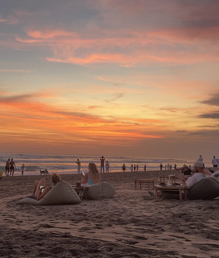 Golden sunset over Canggu Beach in Bali, with surfers in the distance and waves gently rolling onto the shore.
