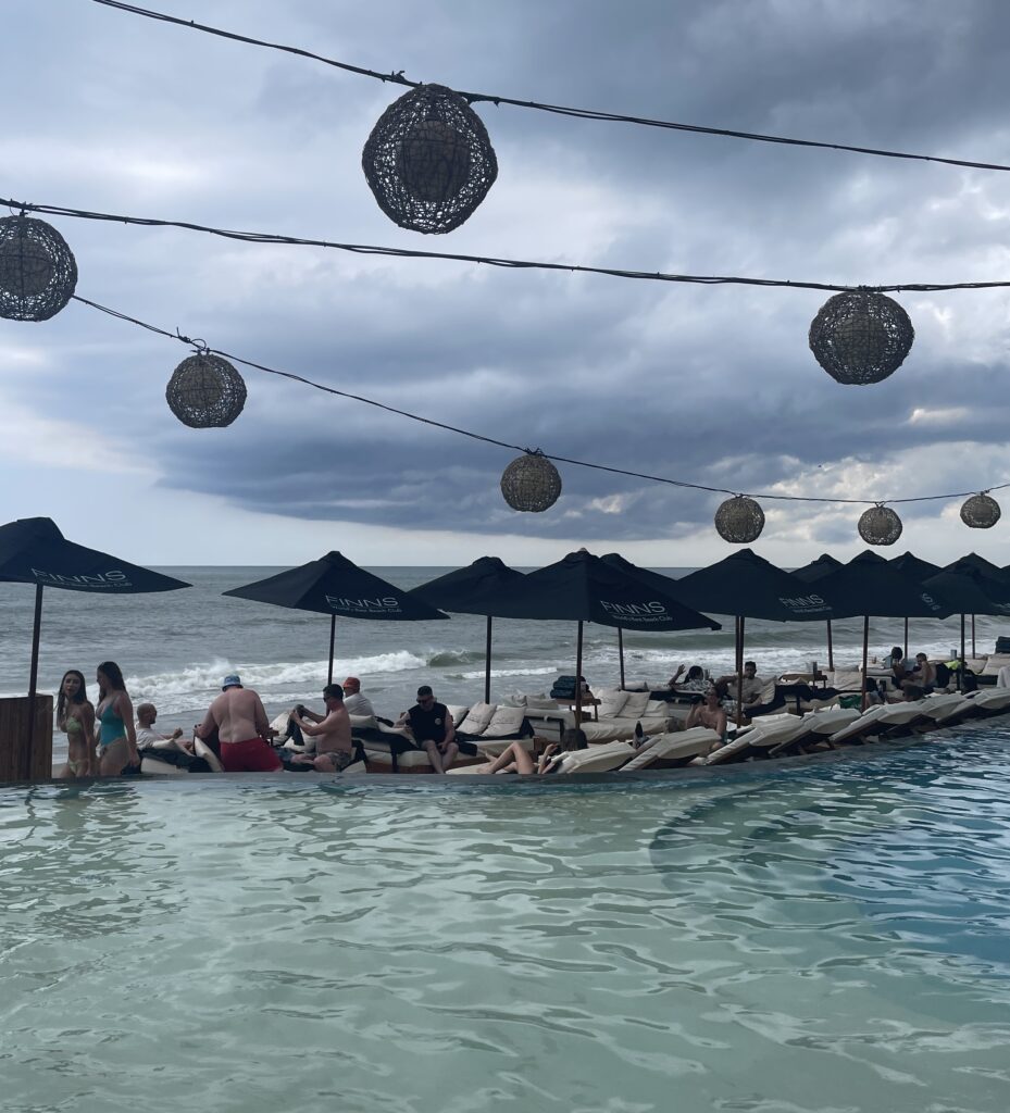 People are sitting on the edge of a pool with umbrellas in Bali during cloudy weather