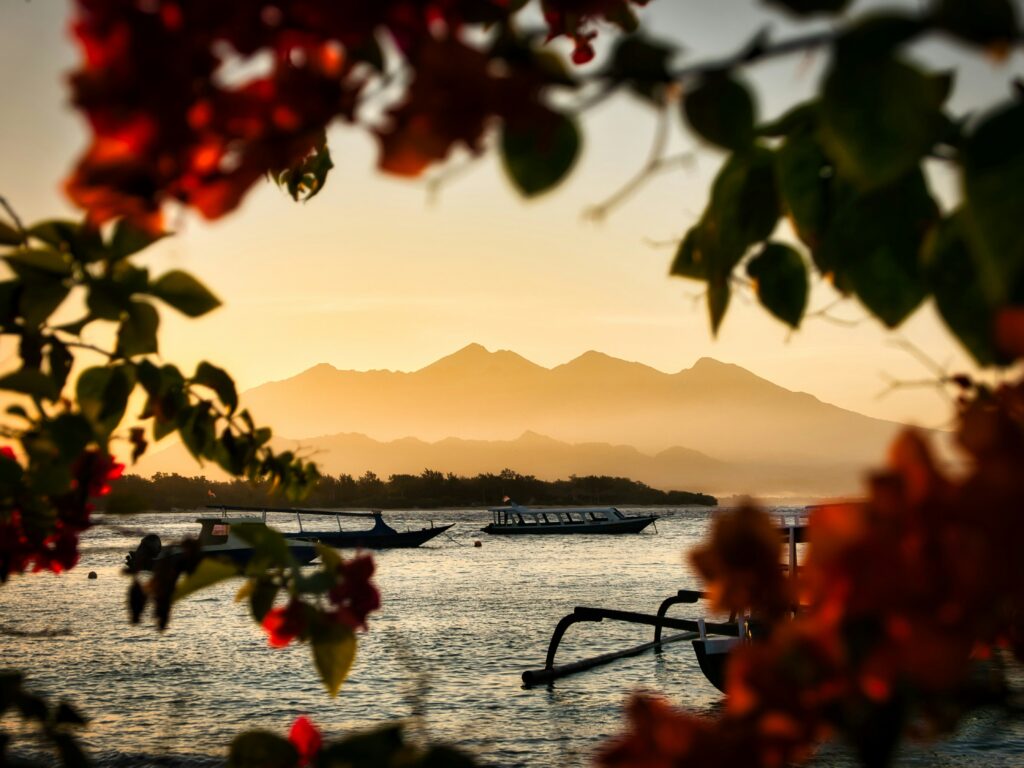 Scenic sunset at the Gili Islands with boats anchored in the water and a mountain silhouette in the background