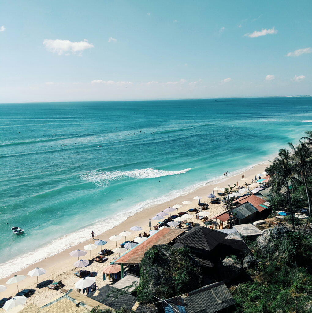 Relaxing scene at Kuta Beach in Bali with clear blue water, rows of beach loungers, and a laid-back resort vibe perfect for sunbathing and ocean views.