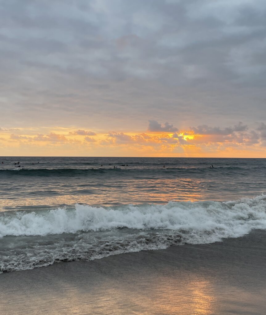 Sanur Beach sunset in Bali Indonesia with golden skies, calm ocean waves, and a peaceful shoreline scene.
