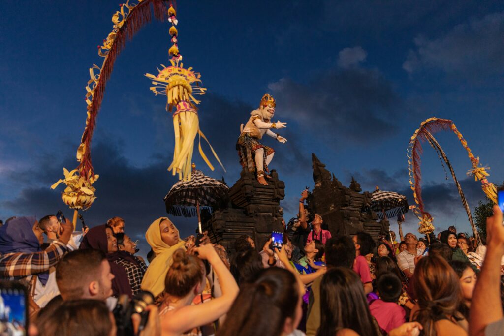 Traditional Kecak fire dance at Uluwatu Temple in Bali with a dramatic sunset backdrop over the ocean.