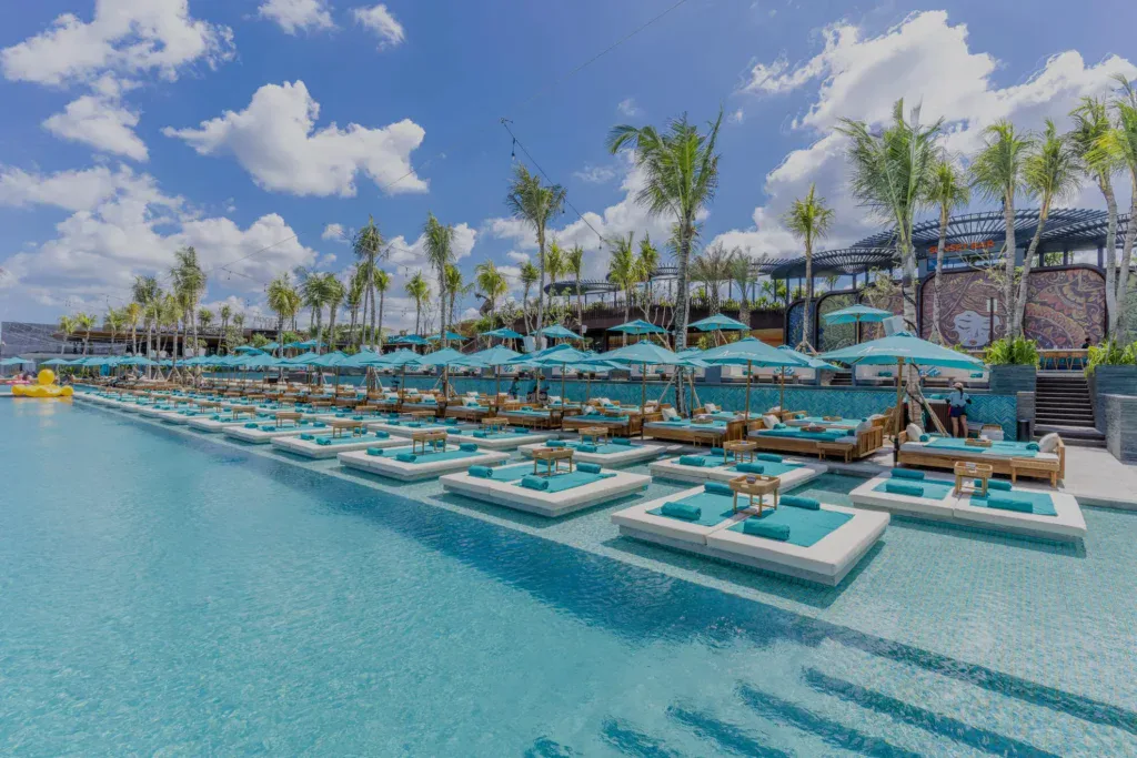 Sunny day at Atlas Beach Club Bali with rows of poolside sunbeds and palm trees