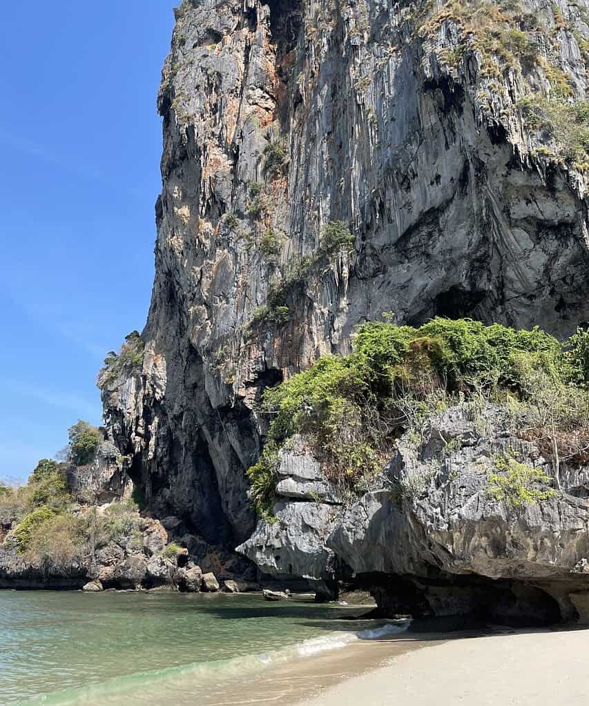 Phra Nang Cave Beach in Krabi with large limestone cliffs, clear water, and sunny skies