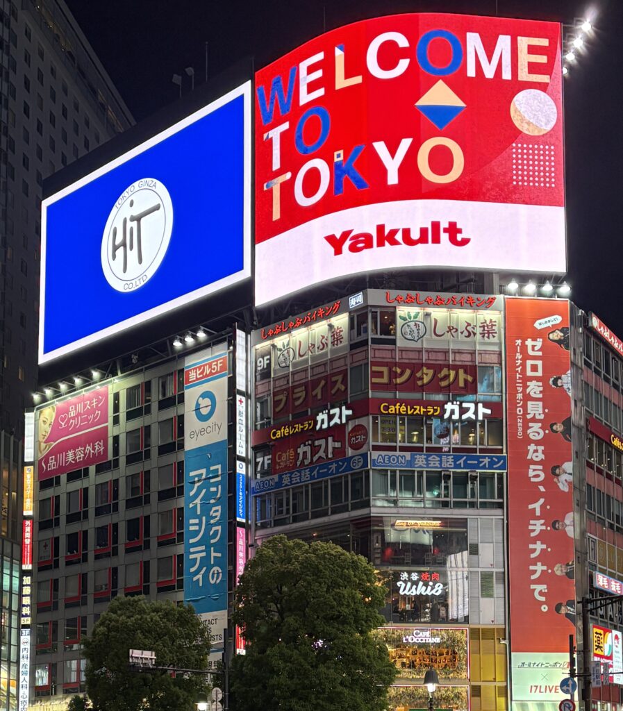 Nighttime view of Shibuya Square in Tokyo with bright neon signs and busy pedestrian crossing