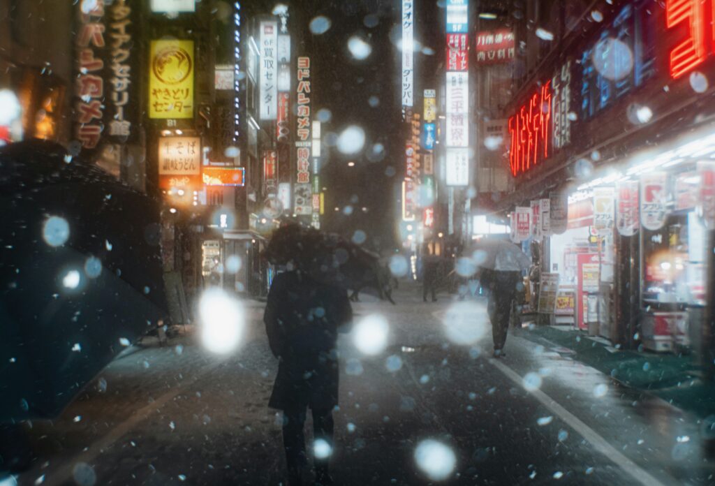 Snow falling over Golden Gai in Shinjuku with glowing bar signs and blurred lights