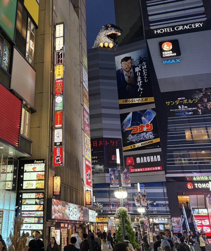 Busy Shinjuku street at night with neon lights and large dinosaur display in the background