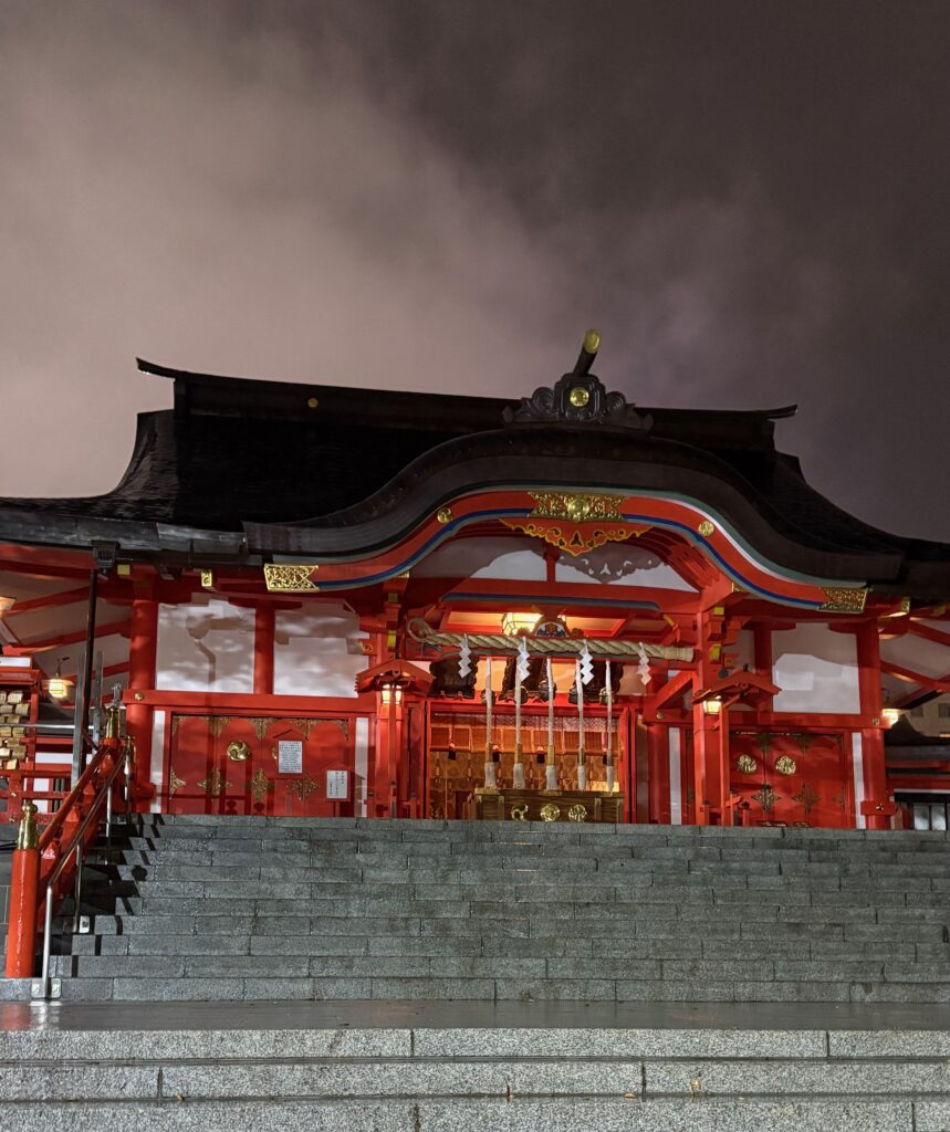 Red temple near Golden Gai in Shinjuku photographed from stone steps under dramatic cloudy skies, capturing the contrast of tradition in Tokyo’s nightlife district