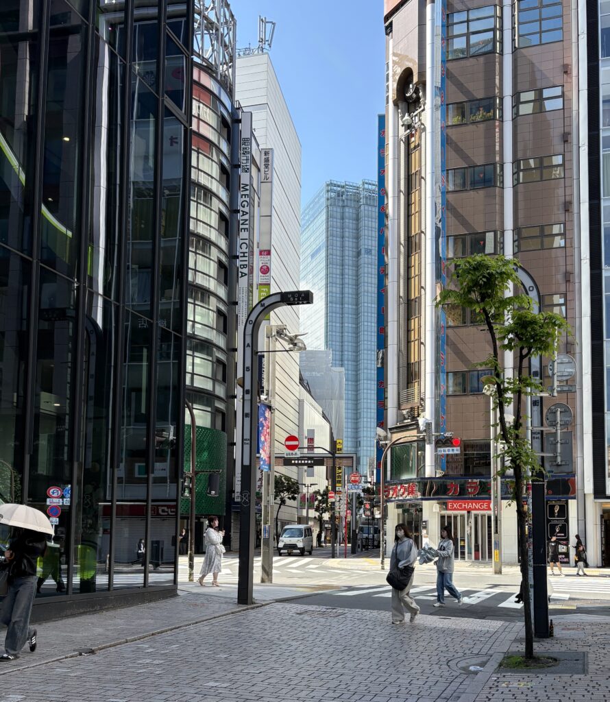 Bright sunny day in Shinjuku with modern buildings and pedestrians walking along a wide pathway