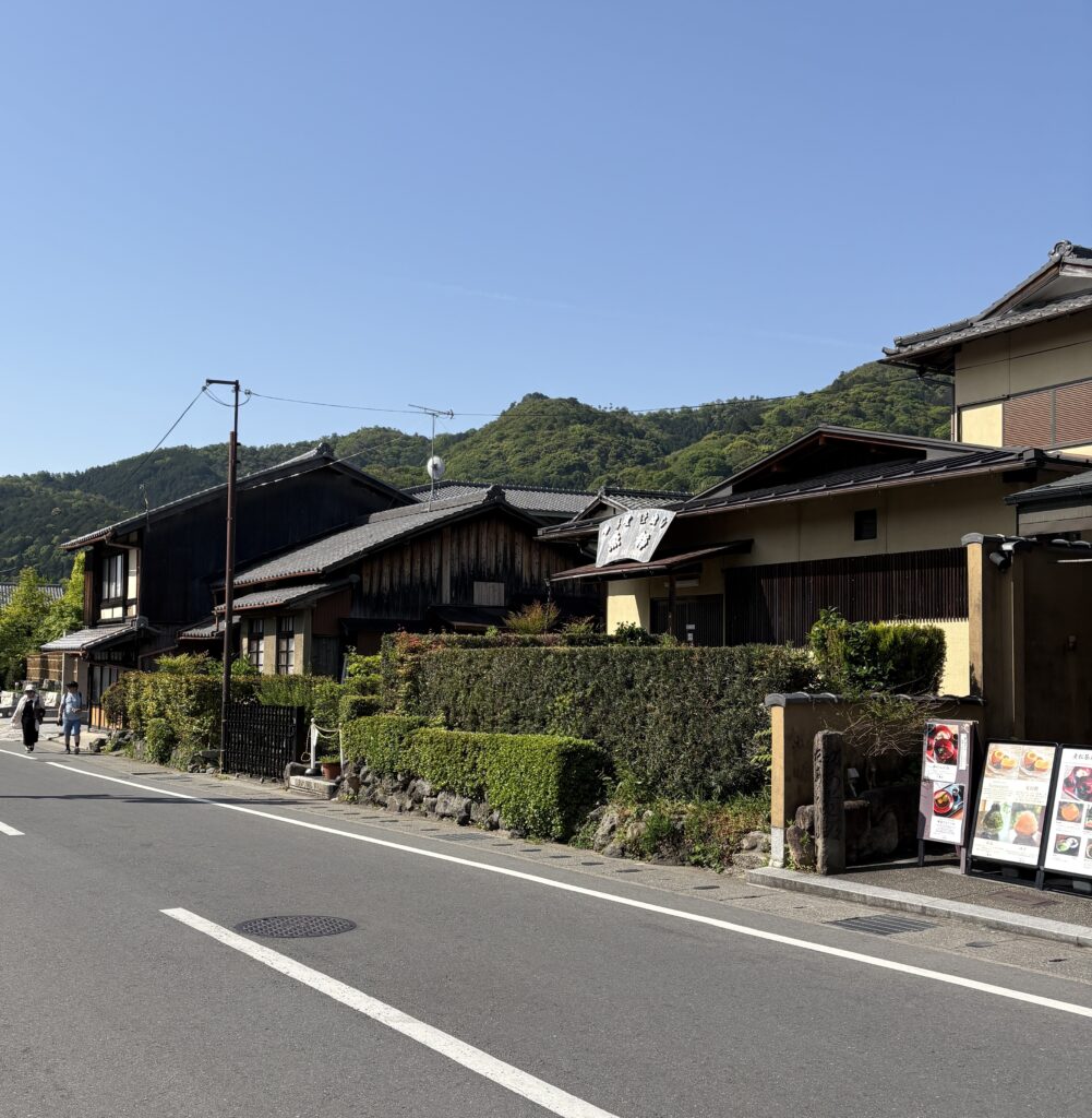 Traditional Japanese restaurants with classic rooftops in Kyoto’s Arashiyama district, set against a lush green mountain backdrop.