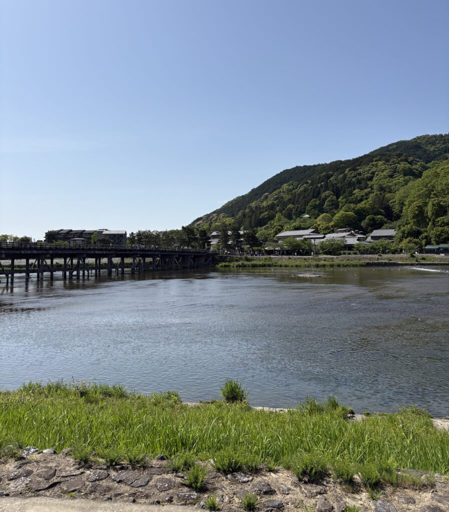 Serene view of the Arashiyama River in Kyoto with lush green mountains in the background and clear blue skies above