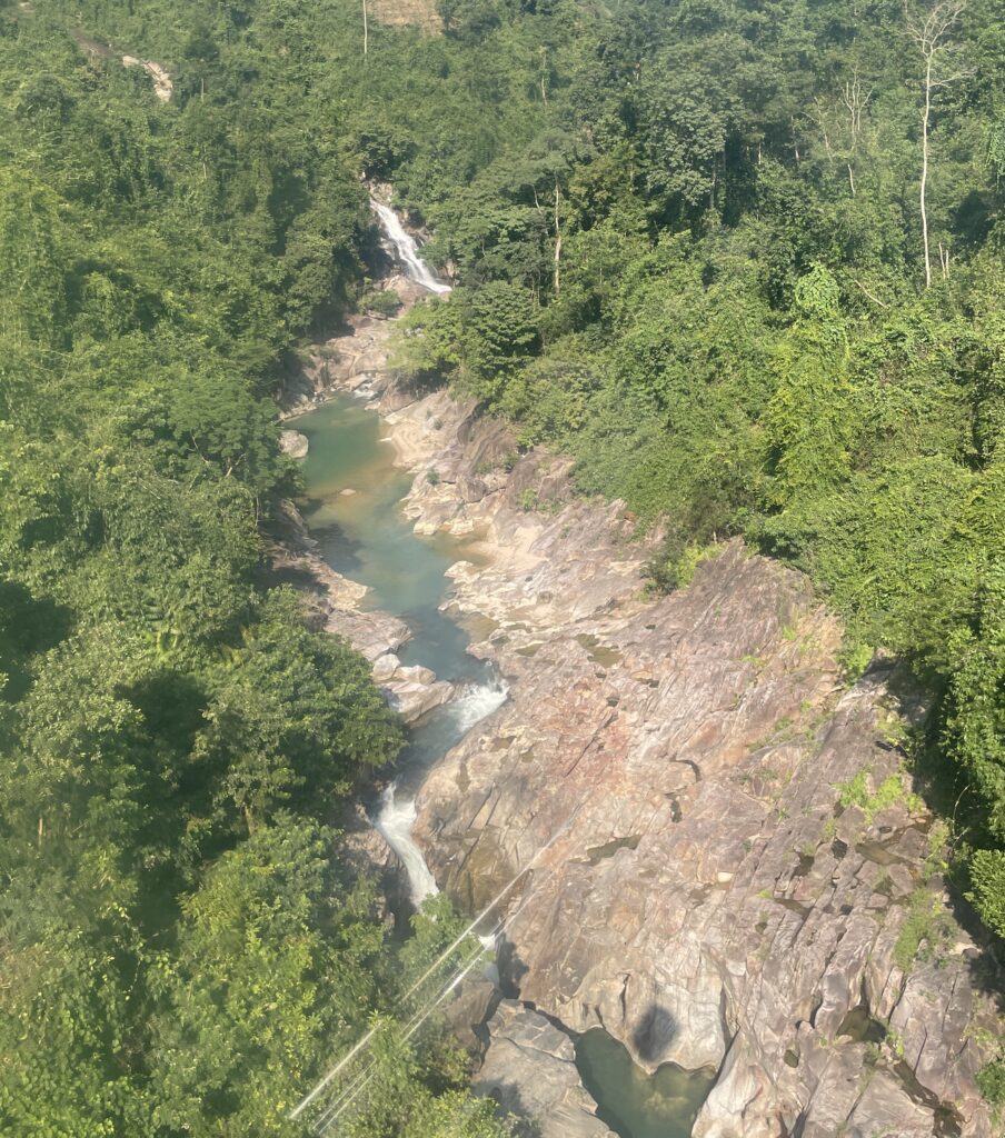 Aerial view from the Ba Na Hills cable car showing lush greenery, winding road, and dense nature below