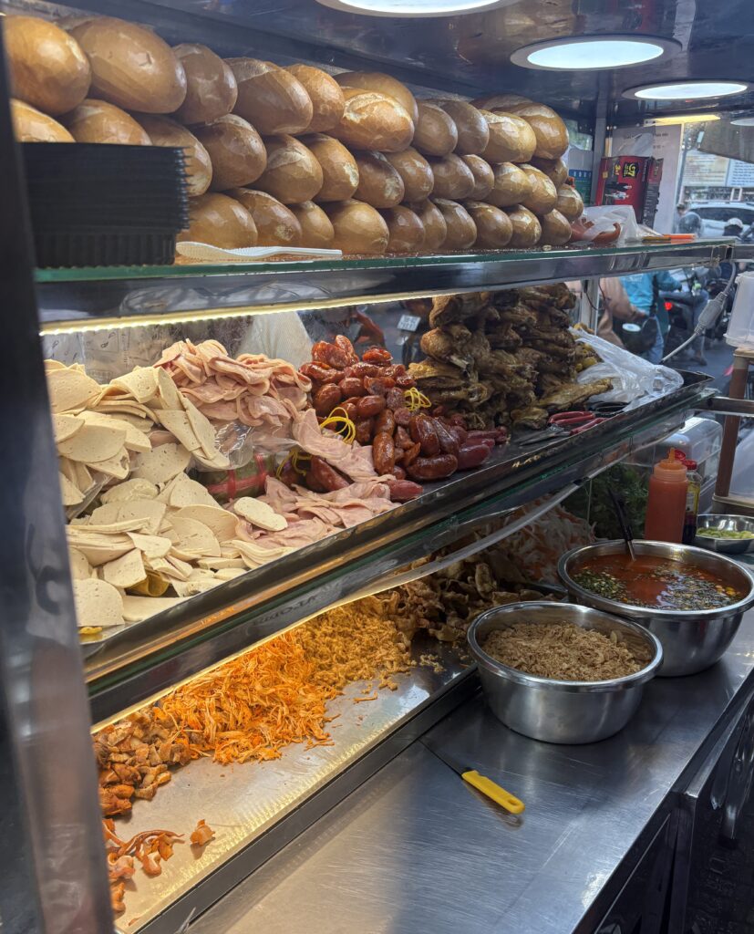 Close-up of a banh mi stall in Ho Chi Minh City with stacked bread and toppings displayed under bright lights