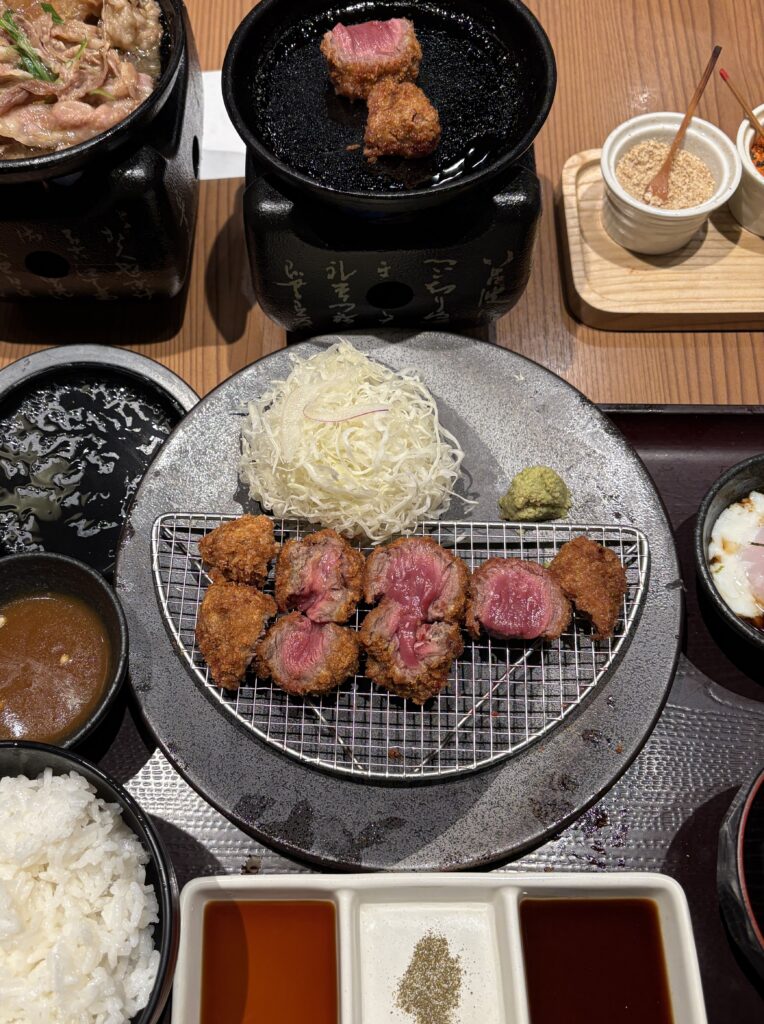 Kyoto-style beef katsu served with salad and sides, with a candle-lit stone grill for cooking at the table.