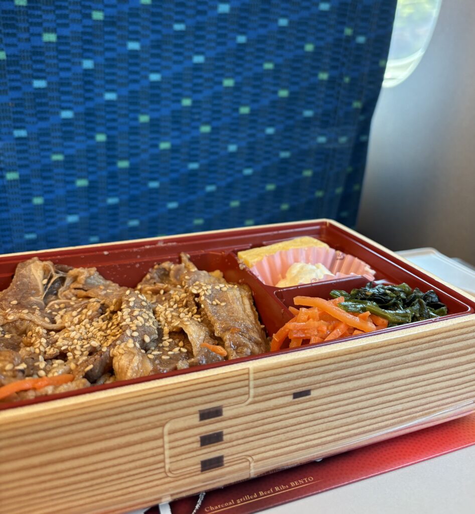 Bento box meal on a tray table aboard a Japanese bullet train with scenic window view