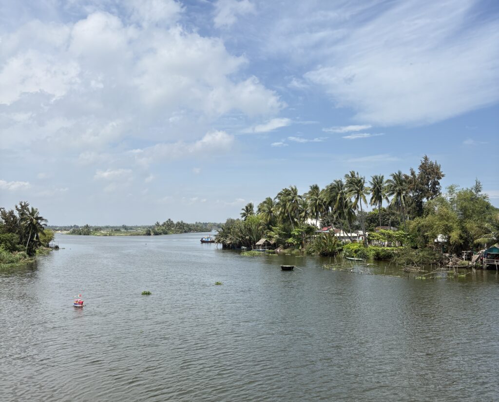 Sunny day view of the Cam Thanh River in Hoi An, Vietnam, with calm waters, palm trees, and traditional Vietnamese basket boats.