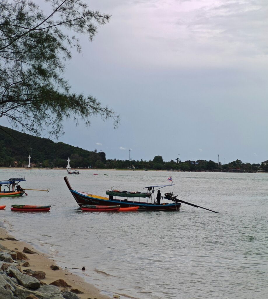 Man navigating a traditional longtail boat across the calm waters of Chalong Bay in Phuket, Thailand
