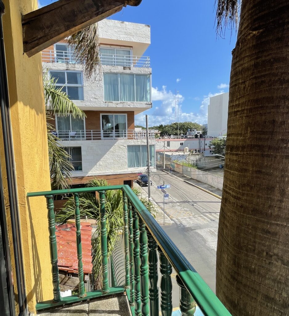 Sunny day view from a balcony overlooking rooftops and palm-lined streets in the Colosio area of Playa del Carmen, capturing the neighborhood’s laid-back vibe.
