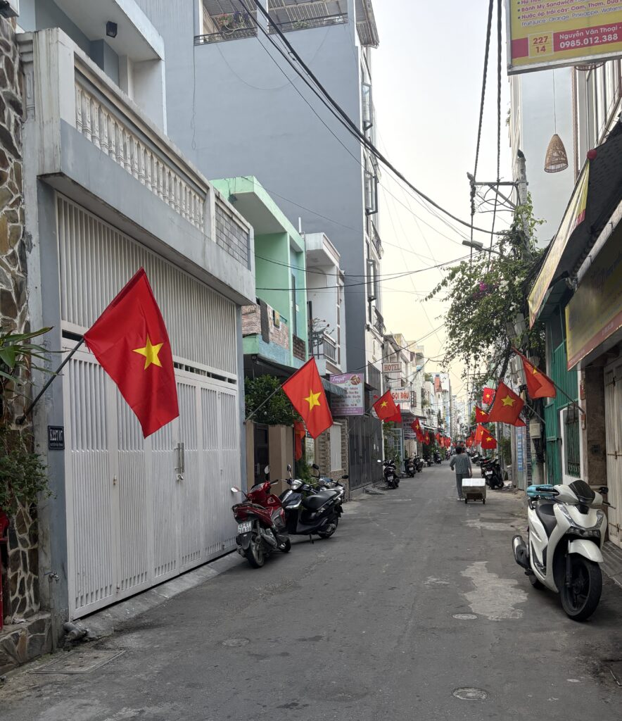 A narrow alleyway in Da Nang lined with Vietnamese flags hanging above the road on both sides.