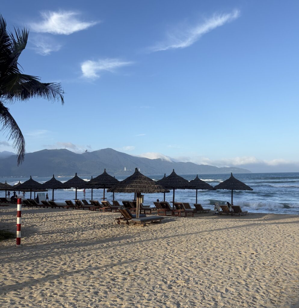 Evening scene on Da Nang beach with rows of beach loungers, clear skies, and mountains in the background.