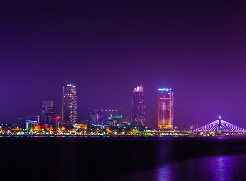Nighttime skyline of Da Nang city center viewed from across the river, with buildings lit up and reflections in the water