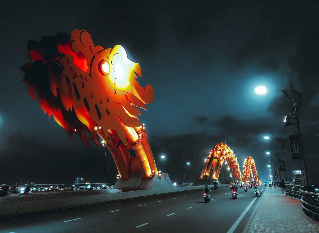 The Dragon Bridge in Da Nang illuminated at night, glowing yellow over the Han River with no fire show visible.