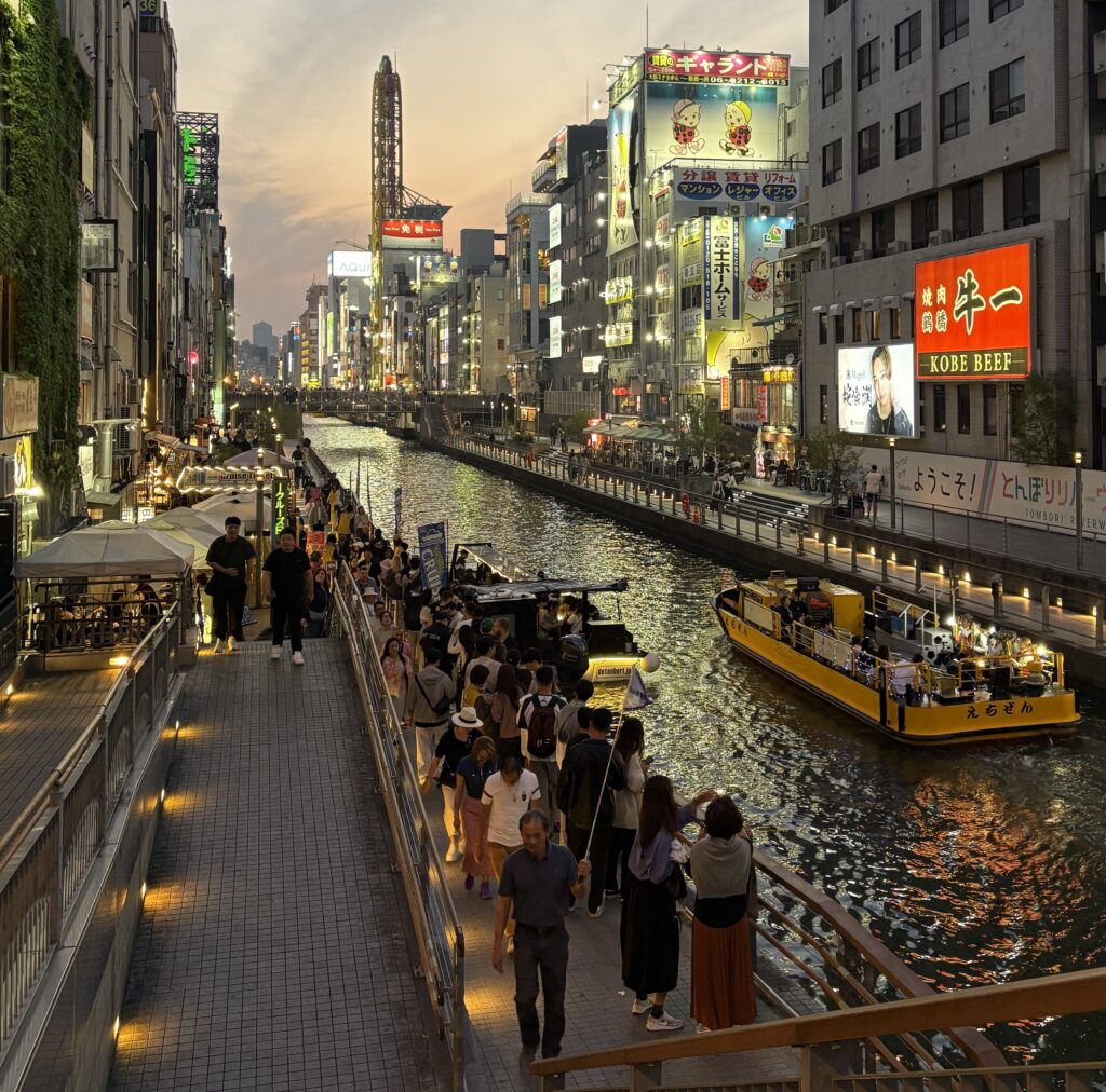 Tourists walking along the Dotonbori river in Osaka with a boat gliding by during golden hour light