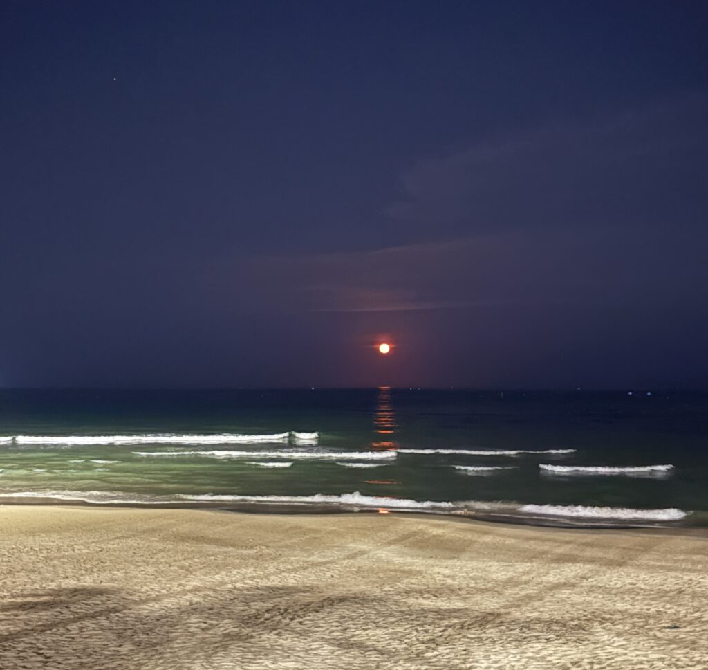 Secluded beach at night between Da Nang and Hoi An, with a glowing red moon over the ocean and no people in sight