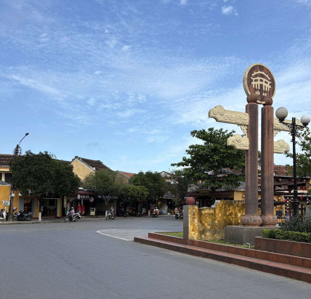 Quiet street in Hoi An’s Cam Pho area featuring a local statue and traditional yellow buildings along the sidewalk.
