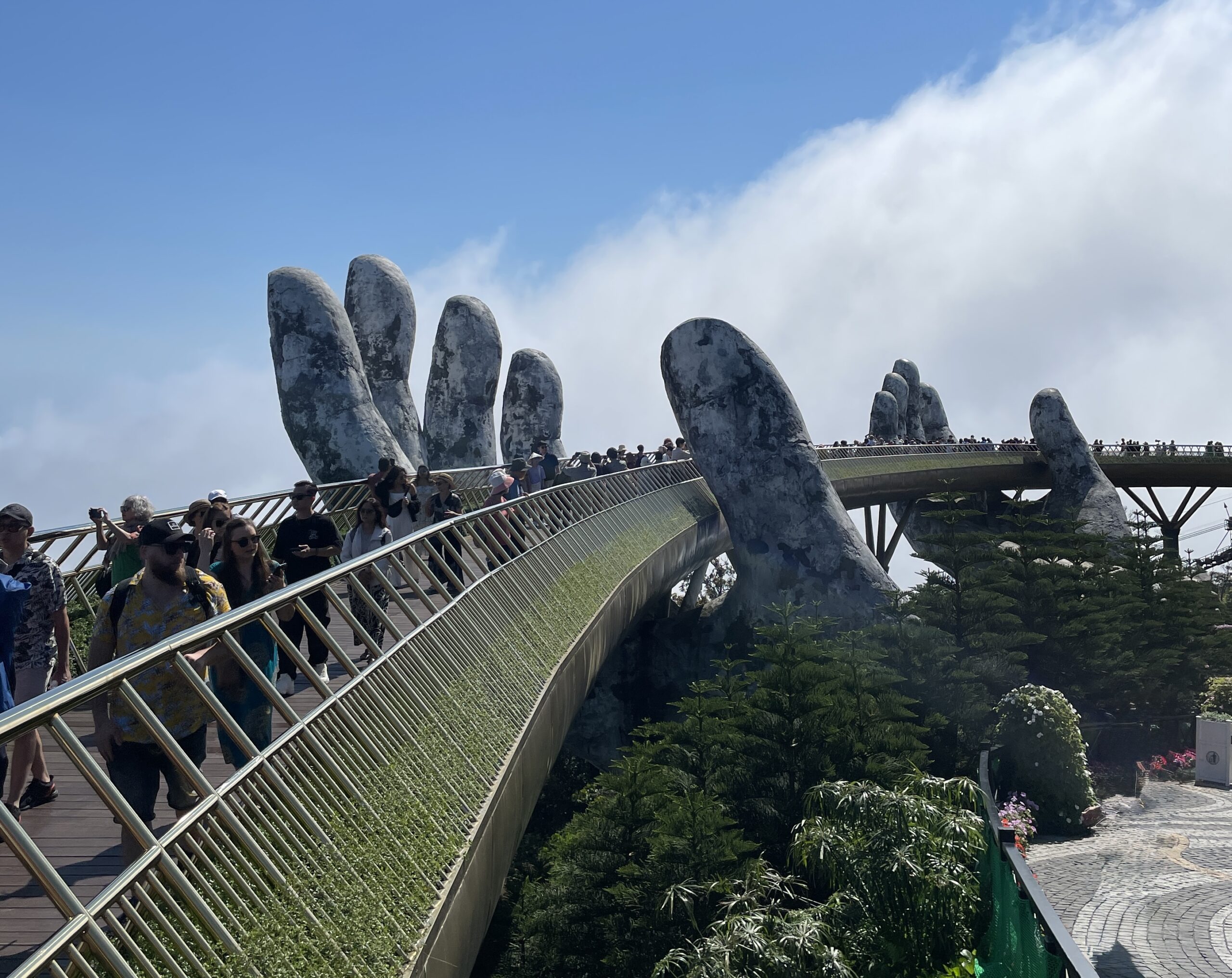 Tourists walking along the iconic Golden Bridge held by giant hands at Ba Na Hills, captured on a clear day in Da Nang.