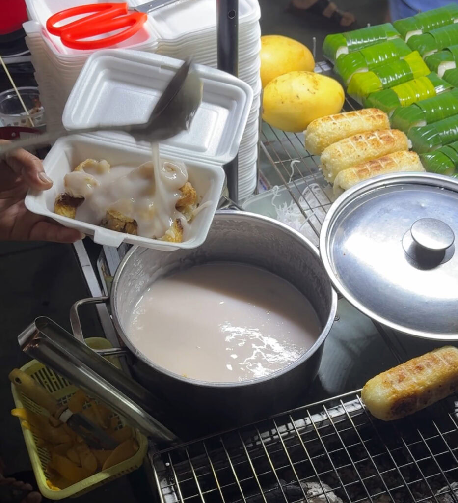 Man serving a crusted grilled banana dessert topped with thick coconut milk in Hoi An Old Town