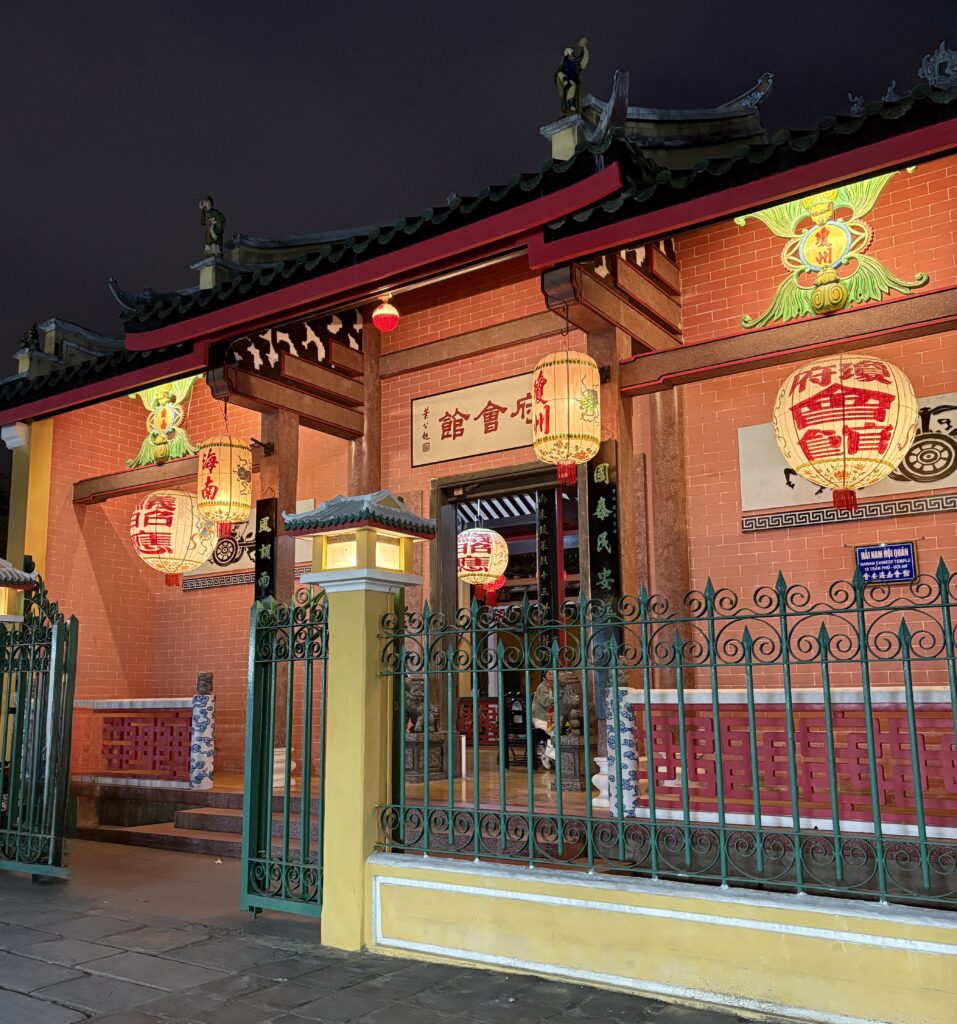 Front of a historic, brightly lit Chinese-style temple at night in Hoi An.