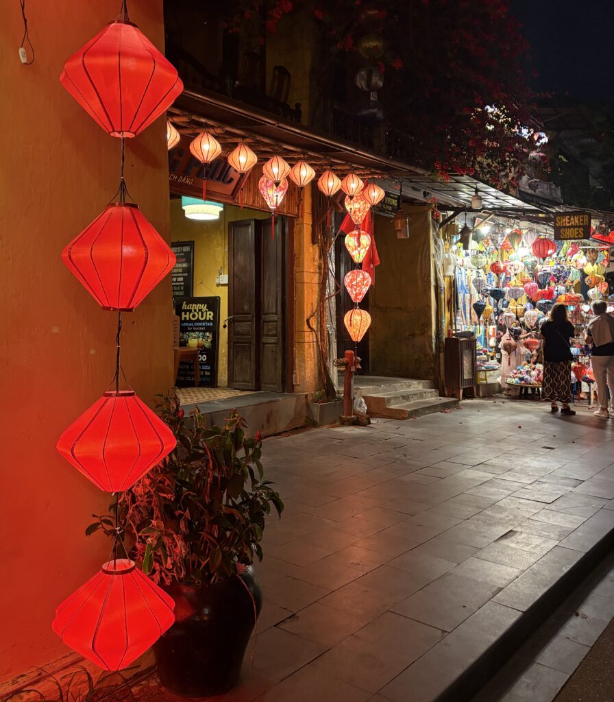 Lantern shop in Hoi An at night with multiple brightly lit red lanterns hanging on the left side.