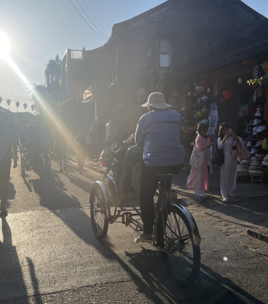 A man rides a cyclo through Hoi An’s Old Town with golden sunset light beaming down the street.
