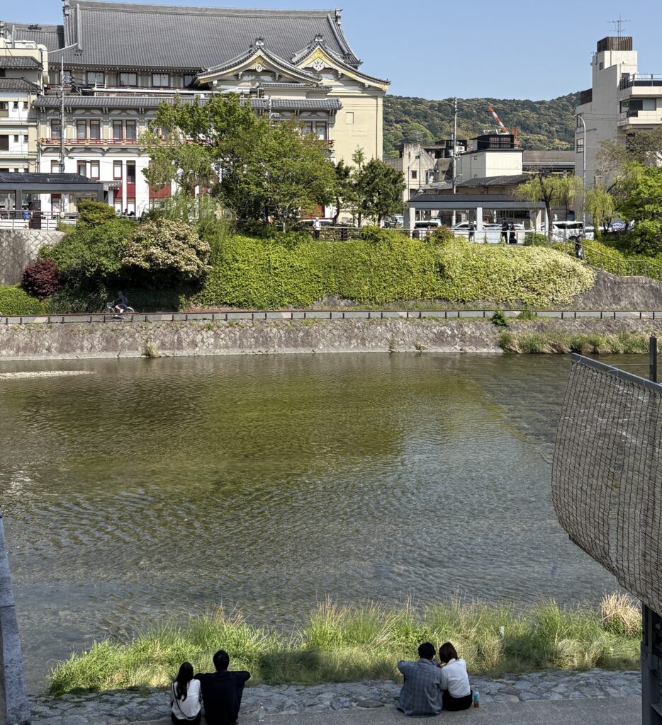 Scenic view of Kyoto’s Kamo River with lush greenery and trees along the riverbanks, and mountains faintly visible in the background