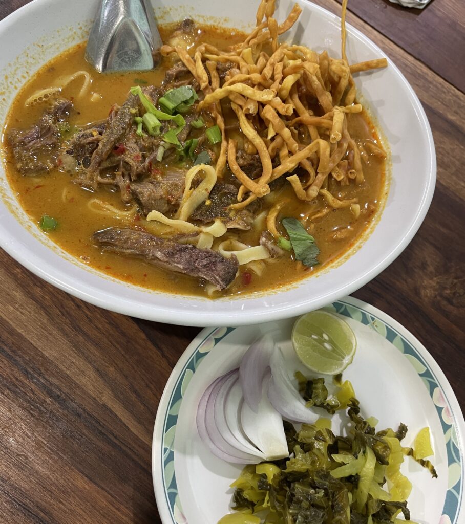 A beautifully plated bowl of Khao Soi with traditional condiments at Khao Soi Lamduan, a Michelin-rated spot in Chiang Mai, Thailand.
