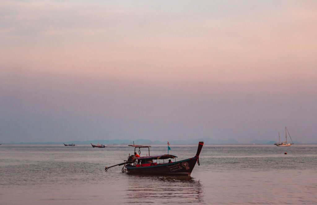 Local man adjusting his longtail boat during sunset with cotton candy skies in Koh Mook, Thailand