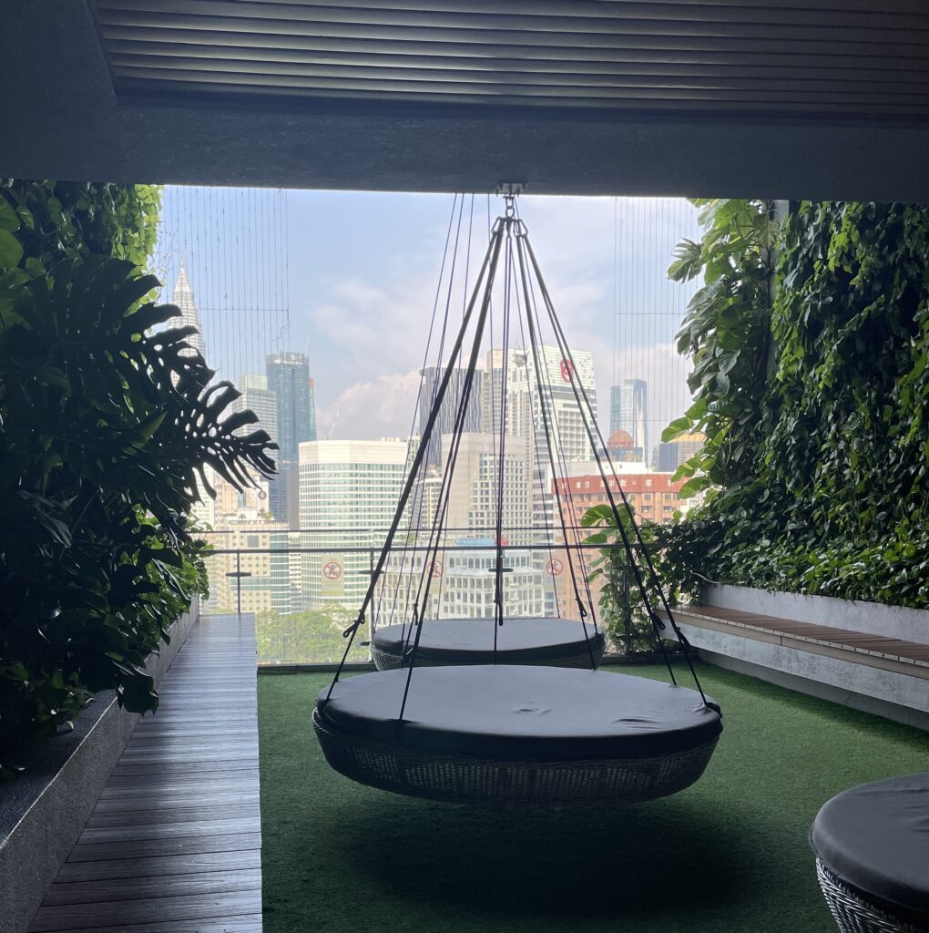 Daytime view of Kuala Lumpur skyline from a hotel rooftop with hanging lounge beds