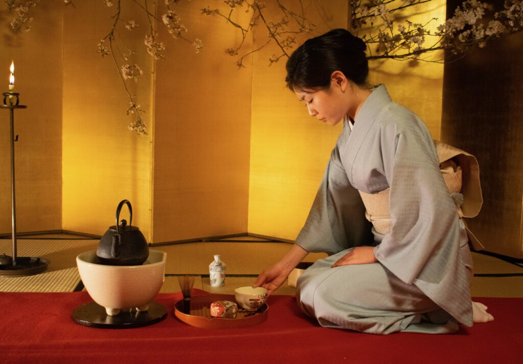 Woman in traditional attire pouring tea during a Kyoto-style tea ceremony, seated in a serene tatami room setting