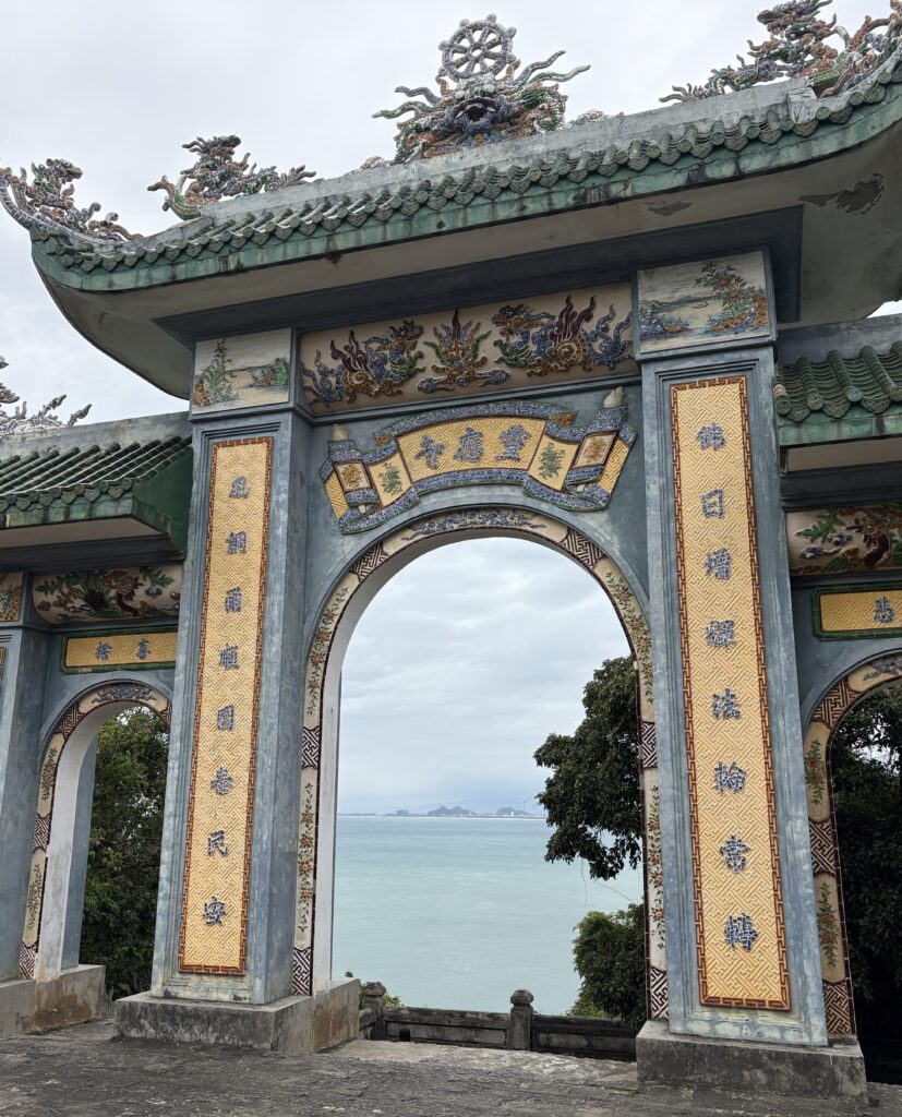 Temple arch at the Lady Buddha statue in Da Nang with panoramic view of the sea and city skyline in the distance
