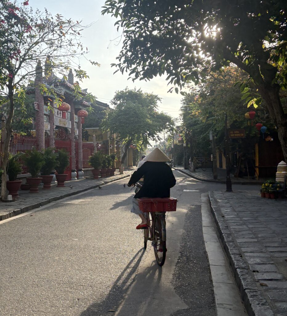 Local woman wearing a Vietnamese hat biking through Hoi An Old Town early in the morning