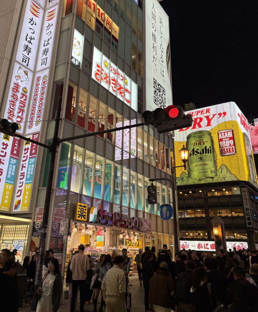 Locals and tourists walking under vibrant billboards at night in the lively Shinsaibashi area of Osaka, Japan