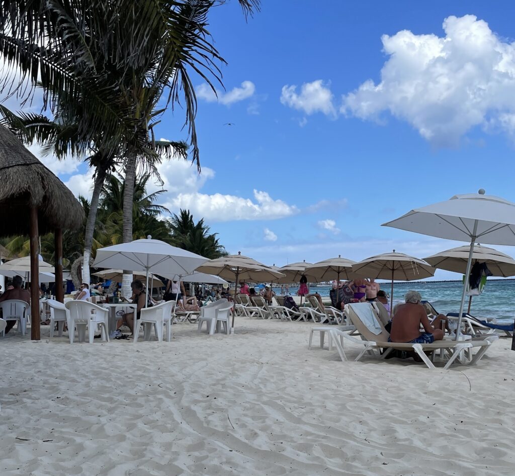 People sunlounging and relaxing on beach chairs in the luxurious Mayakoba area of Playa del Carmen, with beachfront service and a serene ocean backdrop.
