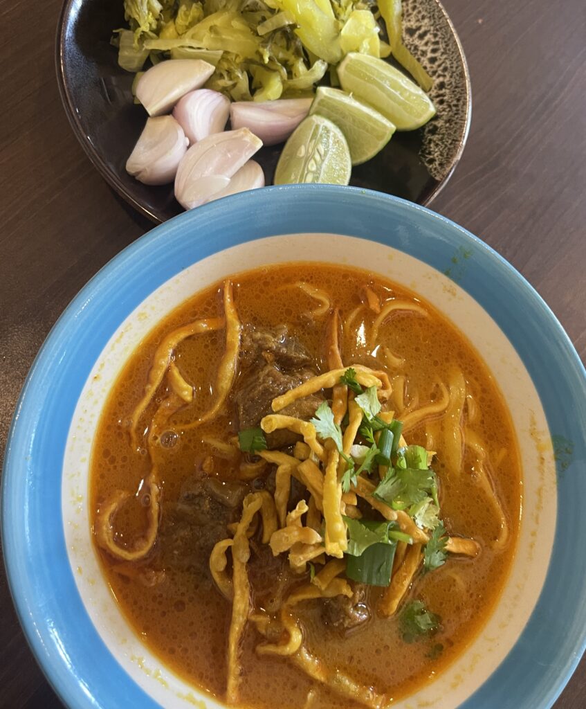 A beautifully plated bowl of Khao Soi with traditional condiments at a Michelin-rated restaurant in Chiang Mai, Thailand.
